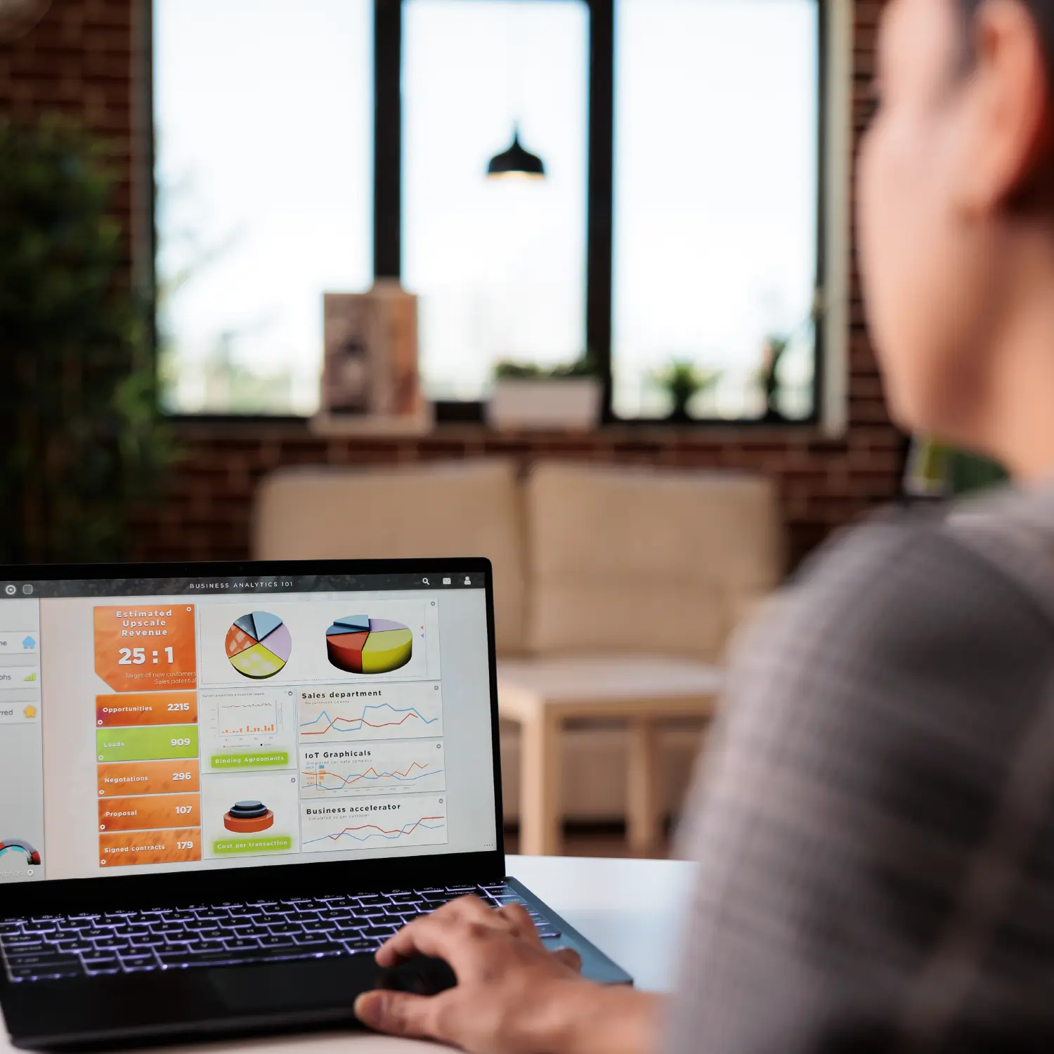 A person sitting indoors, using a laptop on a table with a focus on the screen and touchpad.