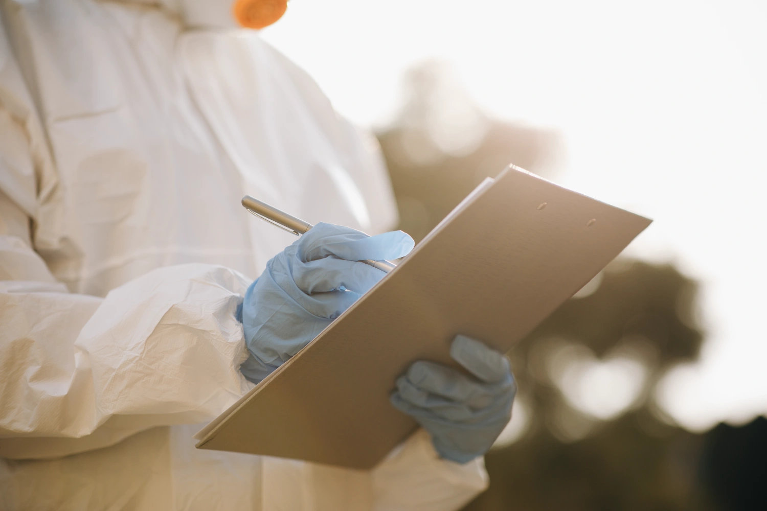 Scientist in full protective suit writing details on a chemical safety data-sheet clipboard