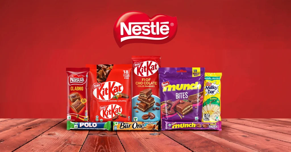 Nestlé chocolate and snack lineup on a wooden table—KitKat, Munch, Milkybar—against a red background.